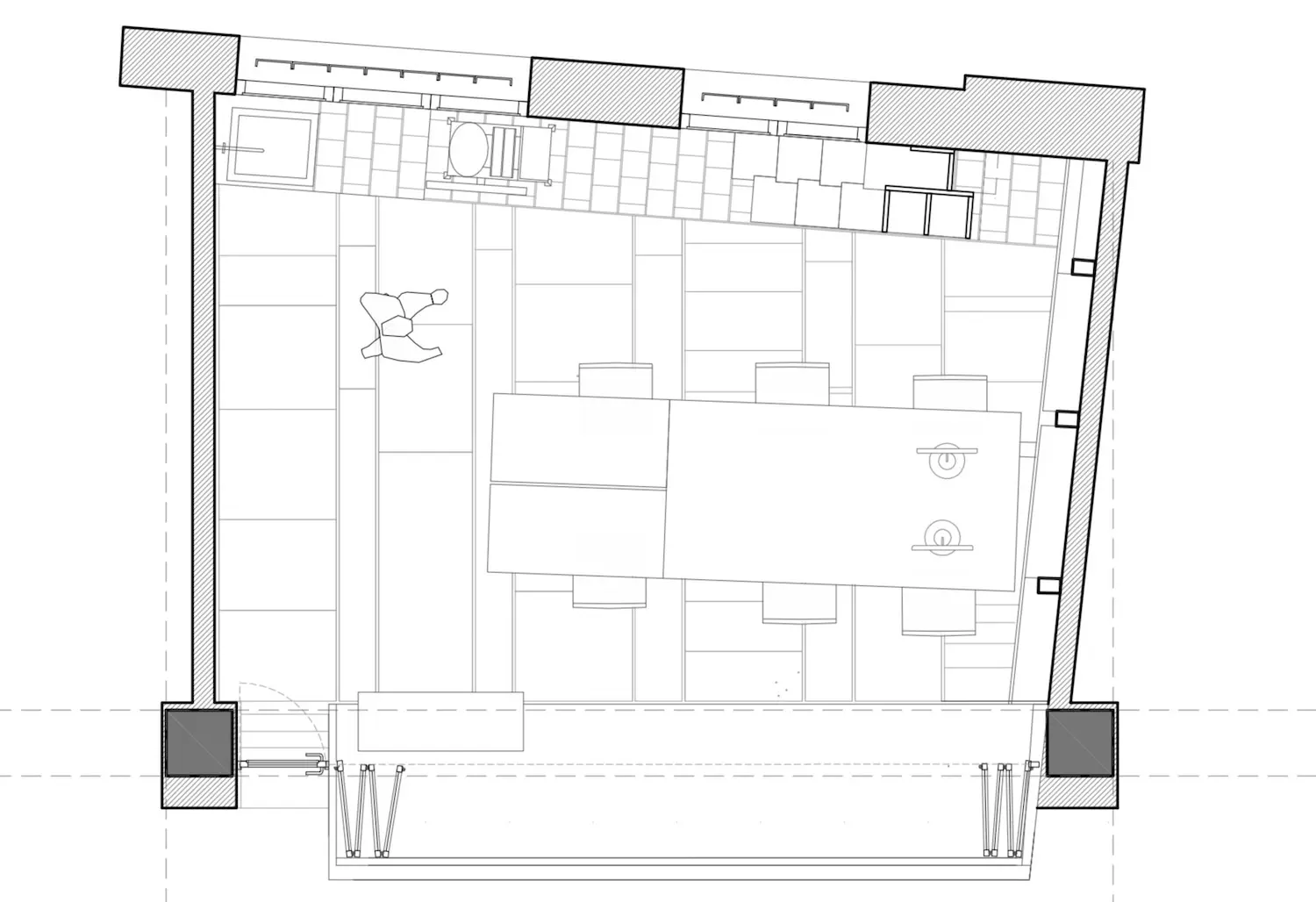 Plano en blanco y negro de una sala con una gran mesa central, varias sillas, una figura que camina y una pequeña zona de aseos en la parte superior. El espacio parece organizado y funcional.