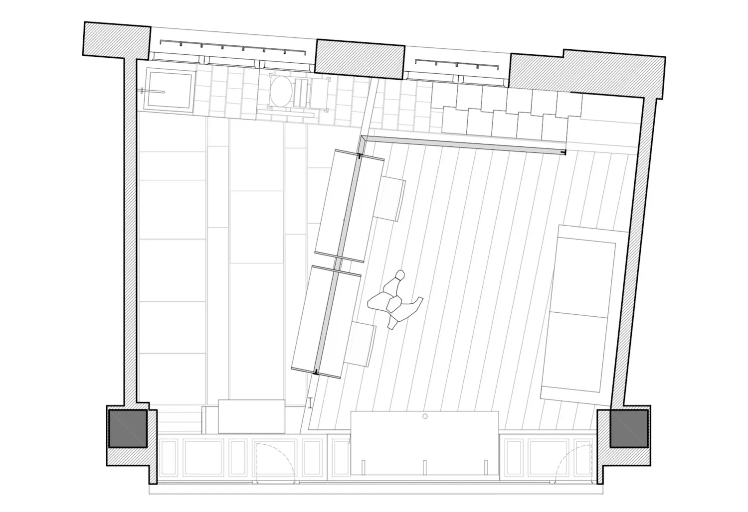 Plano arquitectónico en blanco y negro de una habitación rectangular con zona de cocina, mesa y sillas de comedor, sofá y estanterías. La habitación presenta elementos inclinados y grandes ventanales en uno de los lados.