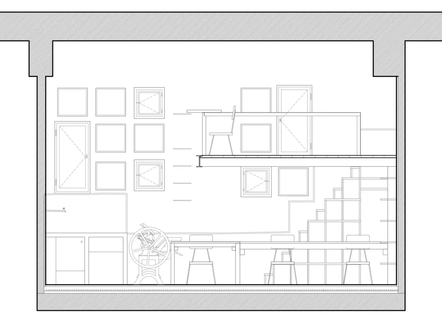 Dibujo arquitectónico en sección de un espacio de trabajo de dos niveles que muestra escritorios, sillas, estanterías, escaleras y múltiples ventanas cuadradas en la pared izquierda; presenta una imprenta en el nivel inferior.