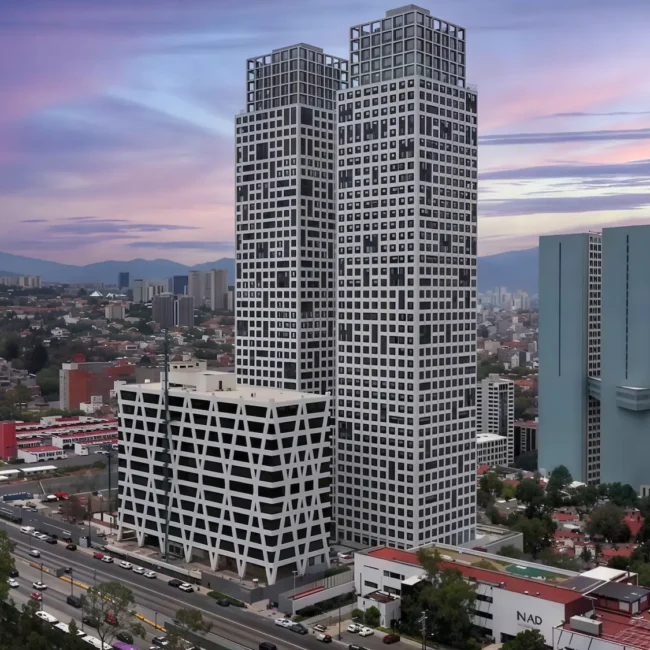 Dos rascacielos altos y modernos con un diseño cuadriculado se sitúan junto a un edificio más bajo de estilo similar. Los coches circulan por la carretera de enfrente, y el paisaje urbano se extiende hacia el fondo bajo un colorido cielo al atardecer.