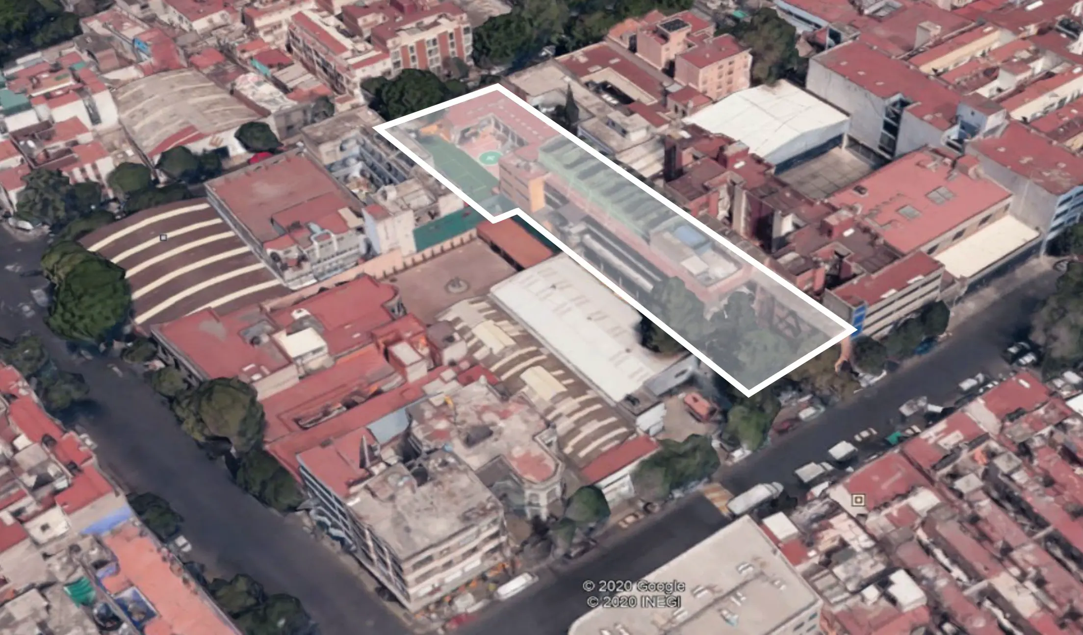 Vista aérea de un barrio urbano con edificios de tejados rojos. Un área rectangular está delineada en blanco, destacando una propiedad específica con algunos árboles y estructuras dentro de ella.